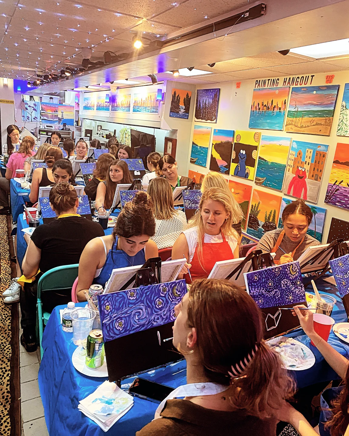 A lively studio class painting under the string lights