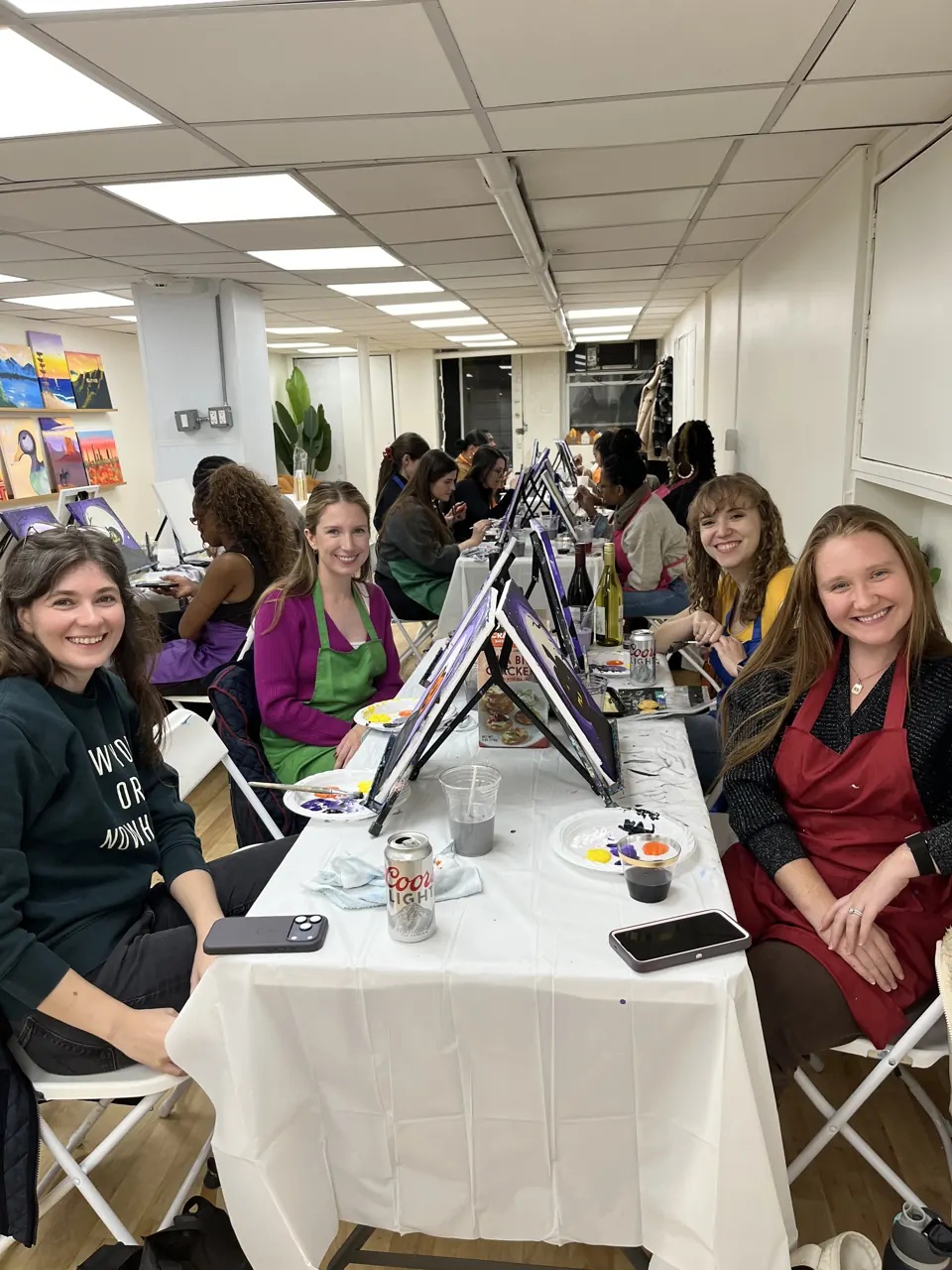 Guests gathered around the studio table painting purple Halloween canvases